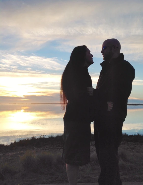 two people standing next to each other near the ocean