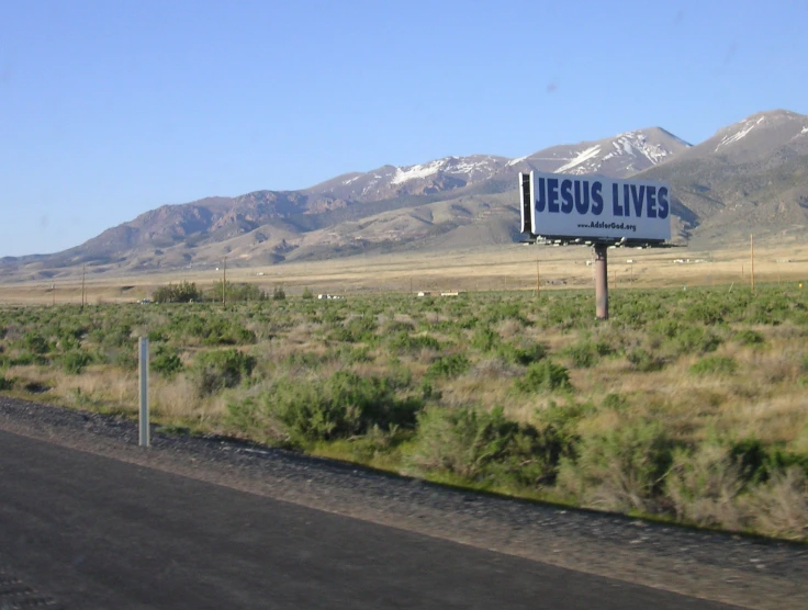 a billboard reads jesus lives with a mountain in the background