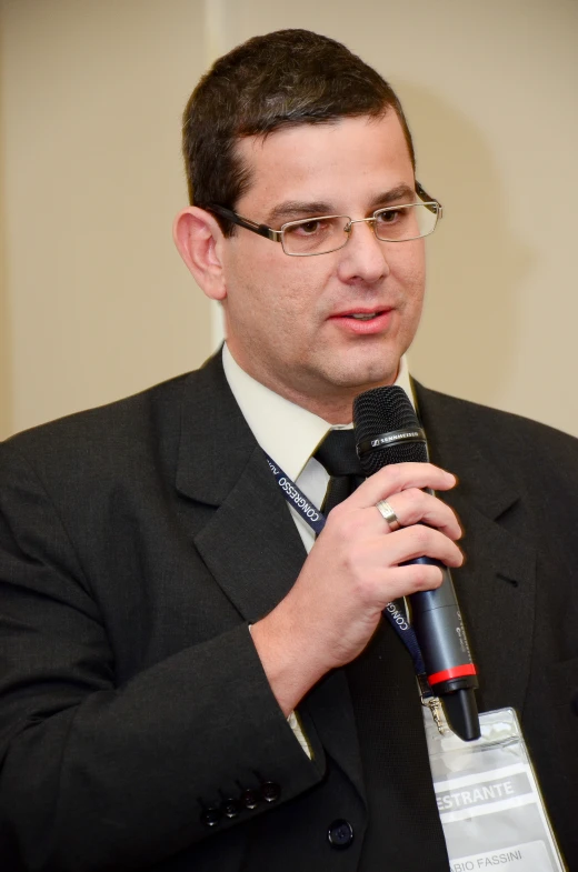 a man wearing glasses and a suit speaks into a microphone