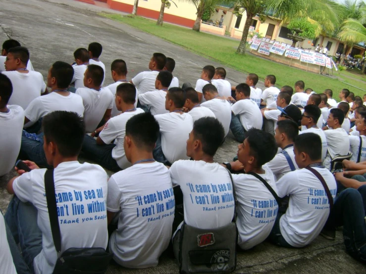 an outside group po of several men wearing t - shirts, one has his back to the camera and sits in front of a crowd