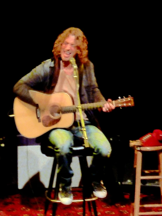 a man sitting down while playing an acoustic guitar