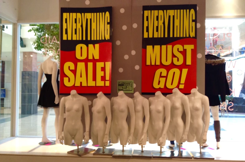 a display window with mannequins dressed in black dress clothing, and advertising signs