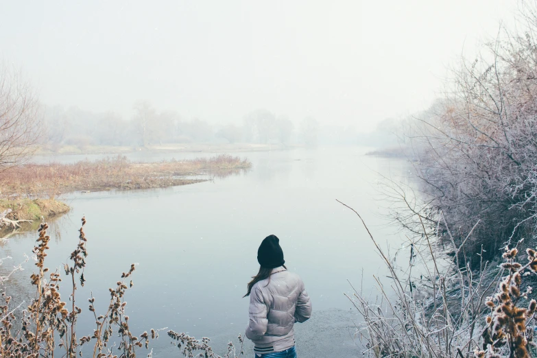 a girl in white jacket standing near water