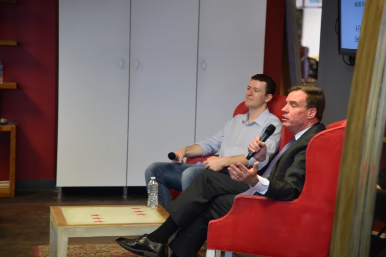 a couple of men sitting down talking in a room