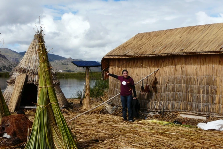 a man stands next to a lake and straw structures