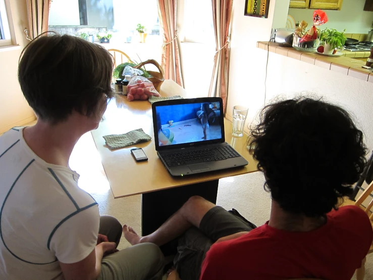 two people sitting at a table, one playing a video game