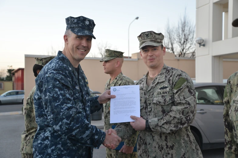 three men in army uniforms smile while shaking hands