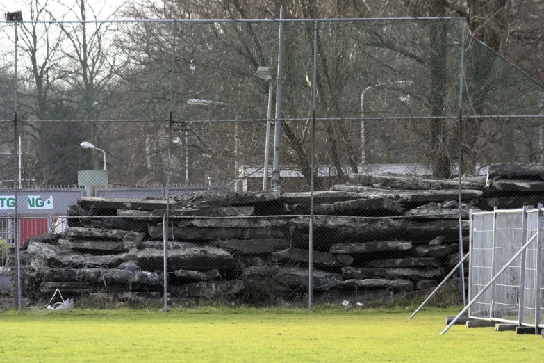 a chain link fence surrounds a field next to piles of logs