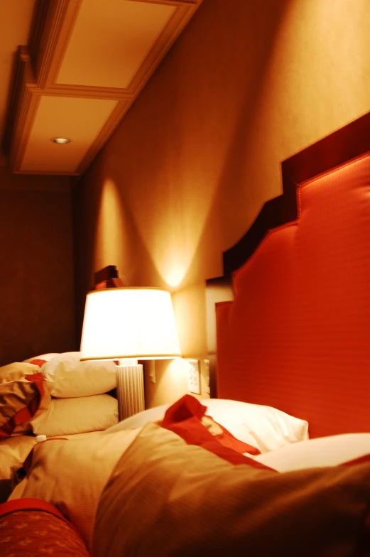 a bedroom with red accents and bedding, a lampshade and headboard