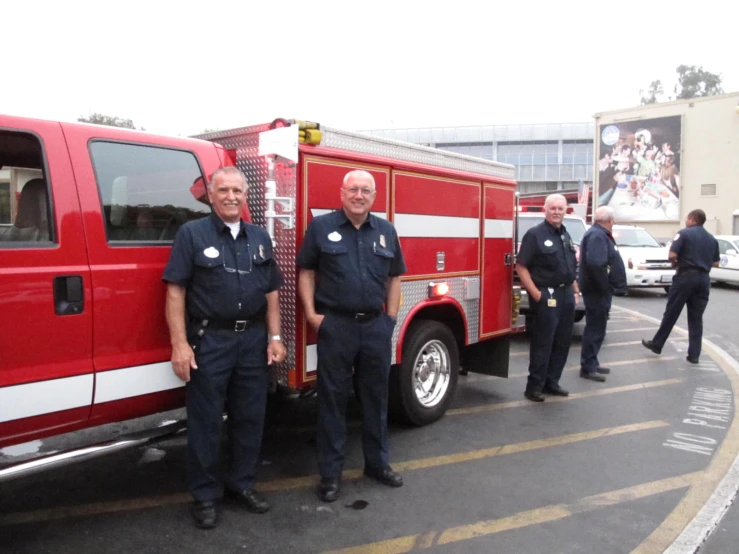 two firemen standing near a red truck with people walking by