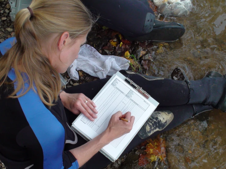 there is a woman sitting in the mud writing on a notebook