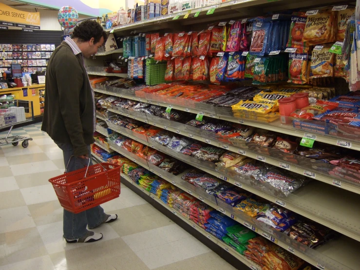 a man standing in a grocery aisle holding a red shopping basket