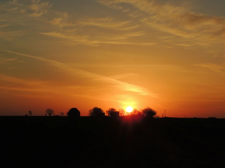 the sun rises over a large field near the horizon