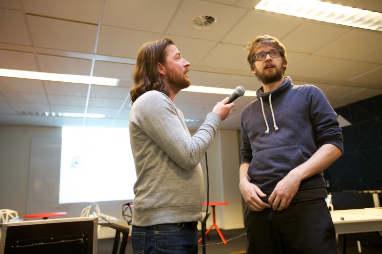 a man with long hair standing next to a man with a microphone