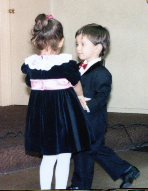 two children dressed in formal dress and bow ties walking together