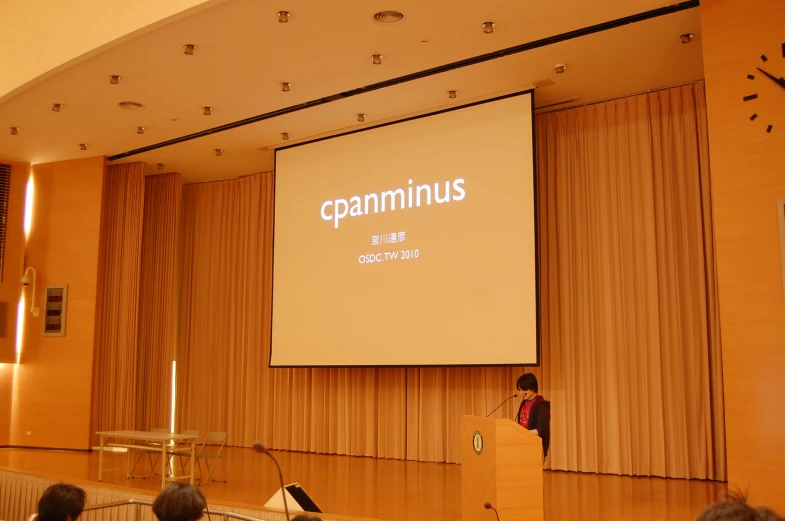 a man on a stage stands near a podium in front of a projected screen