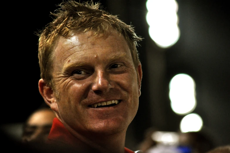 smiling white man in red shirt surrounded by people