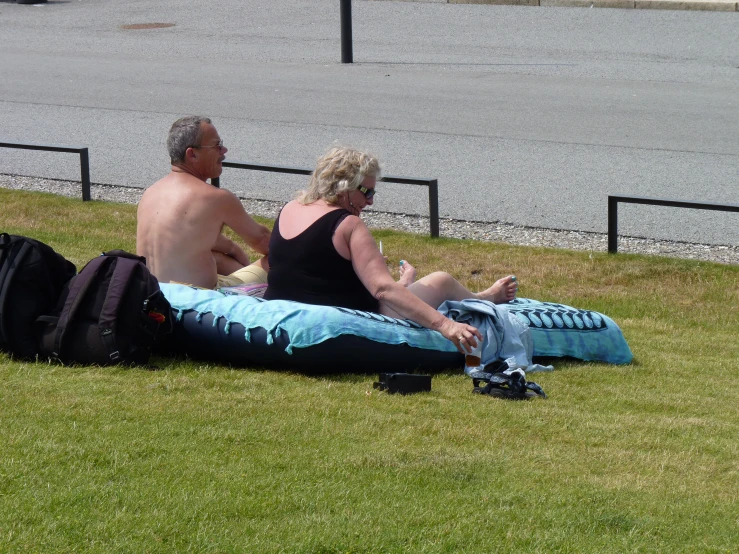 two people sitting on the grass near a road