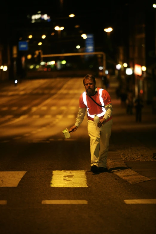 man walking across the street at night with a yellow object