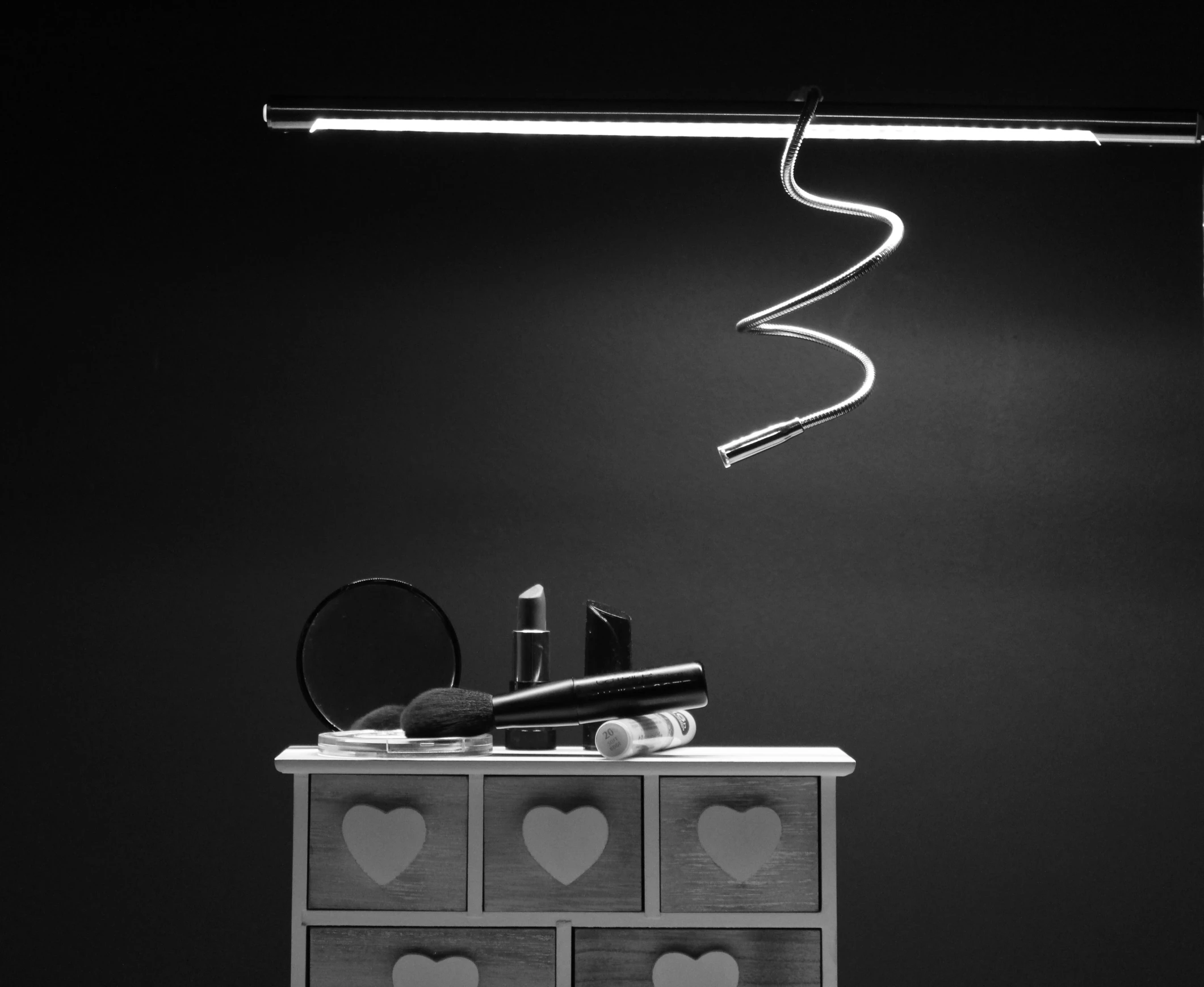 black and white image of lipstick, brush, light strip and mirror