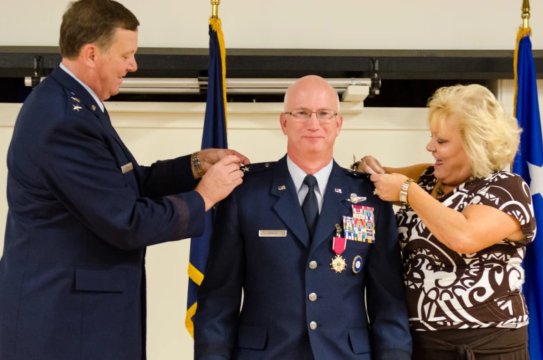 a man in military uniform pinning the medal to a woman