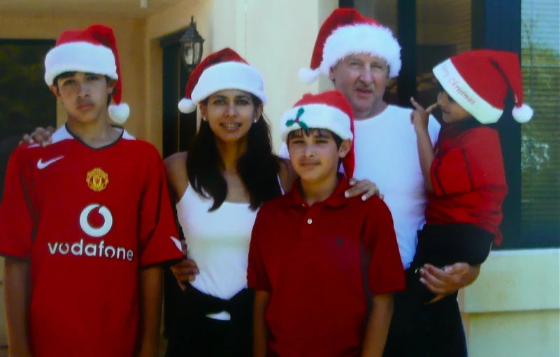 three adults and two children posing for the camera wearing red christmas hats