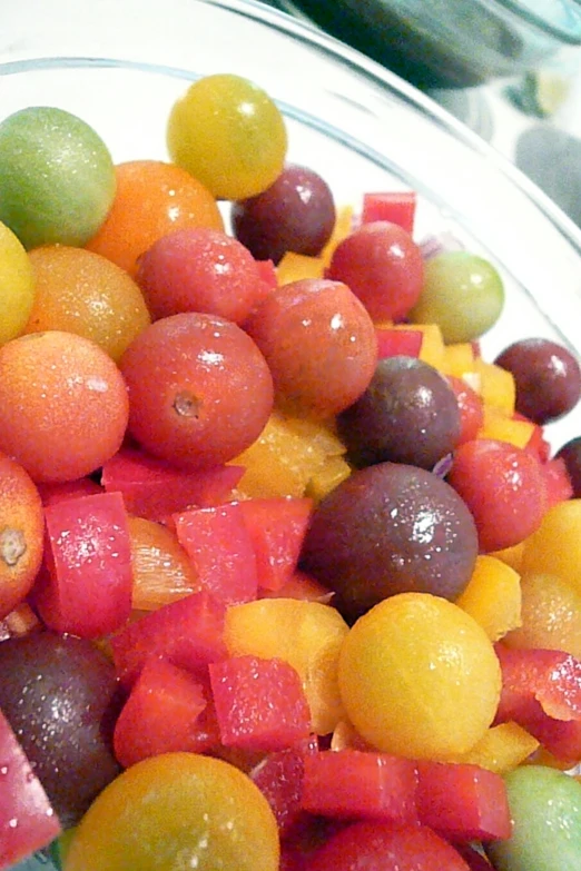 a glass bowl of orange, yellow and red fruit