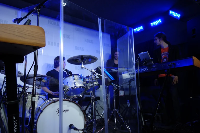 two people and a person sitting at a table in front of a drum set