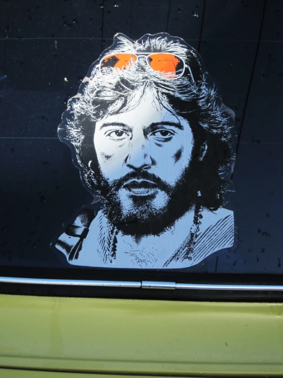 a sticker on the back window of a car with a man in sunglasses on his head and a green pickup truck behind
