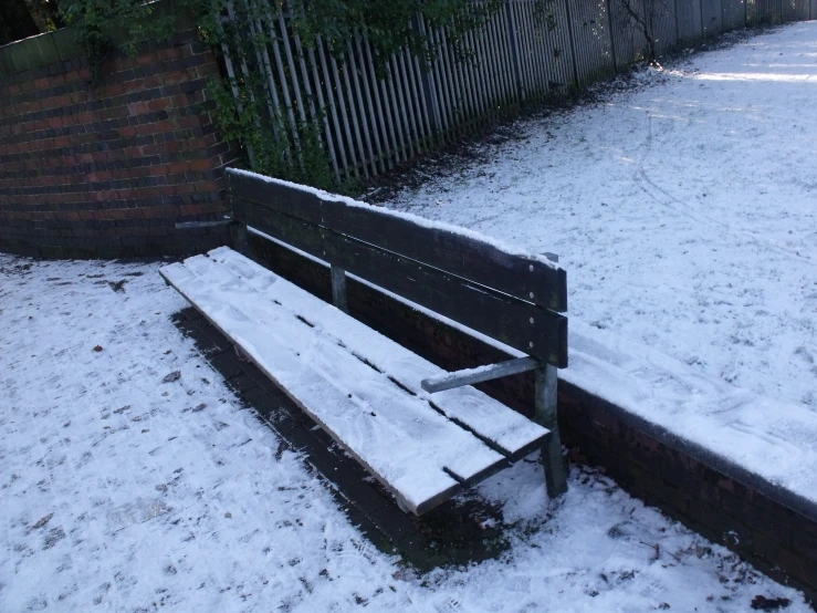 an empty bench sits in the snow beside a fence