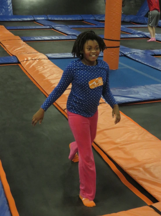 a little girl wearing pink and blue is walking on a trampoline