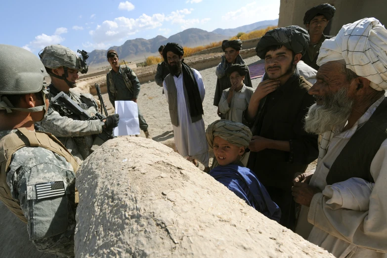 military personnel and civilians standing in an area with sand