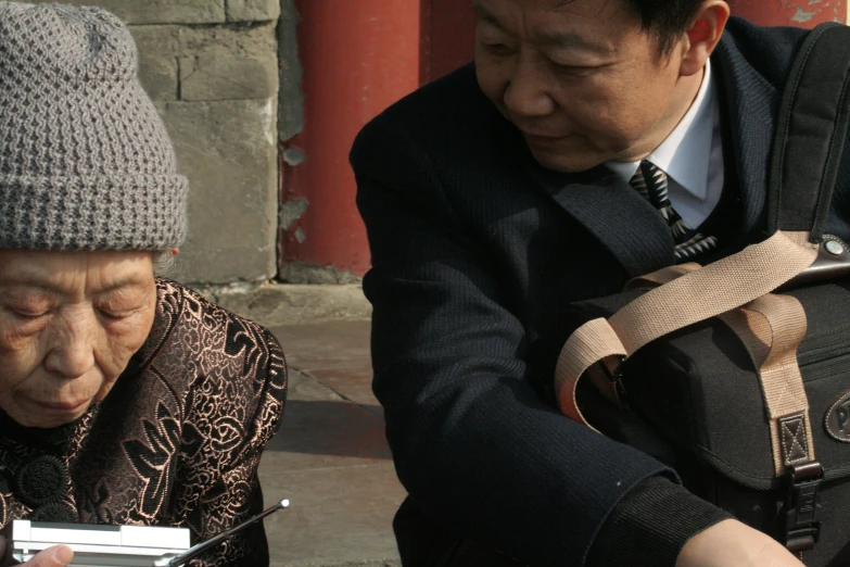 an old man looking at his phone while a man in a grey hat stands nearby