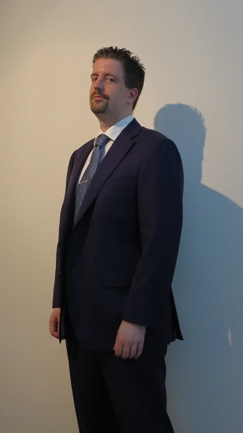 a man standing in a suit against a white wall