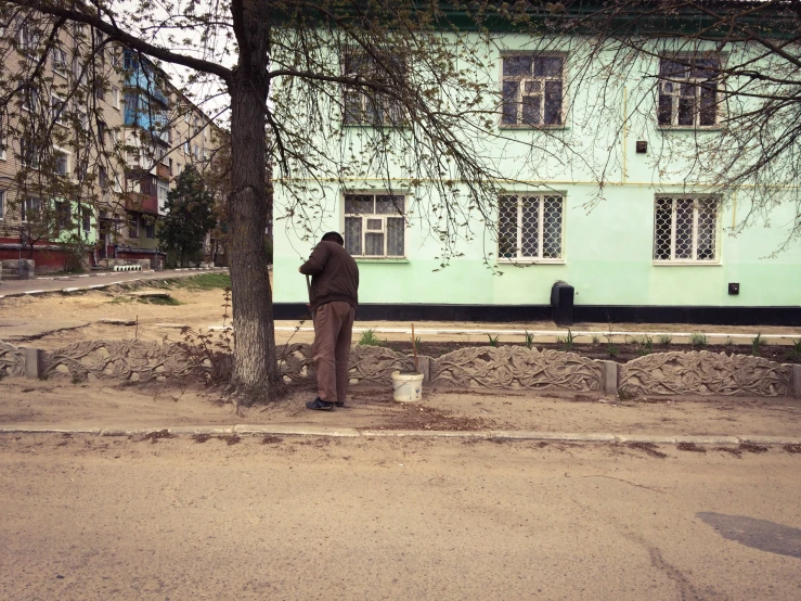 a man sitting on the curb behind a tree next to a house