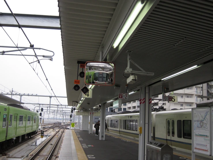 a commuter train pulls into the station while a man in green stands on the platform