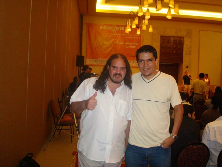 two men pose for the camera in front of some tables