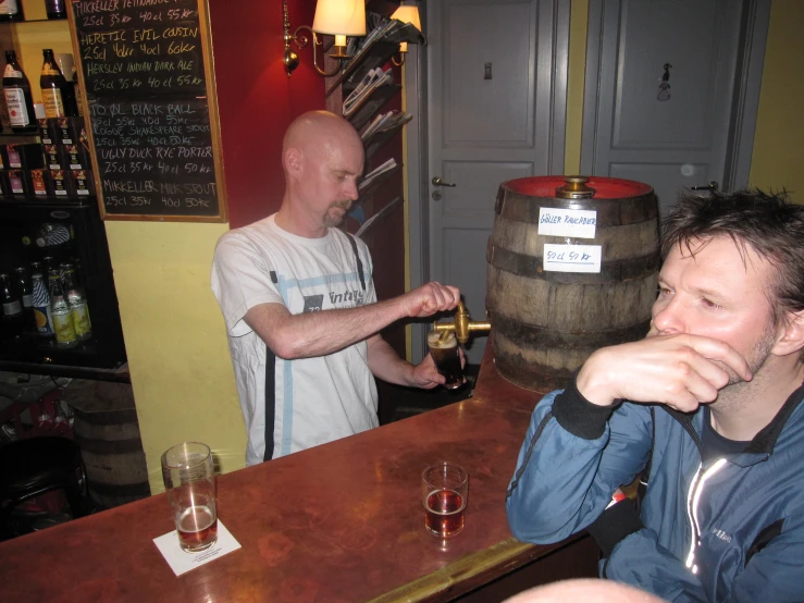 two men standing at a bar, one is holding a bottle