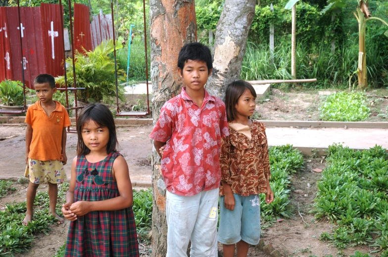 three children stand by a tree outside of their home