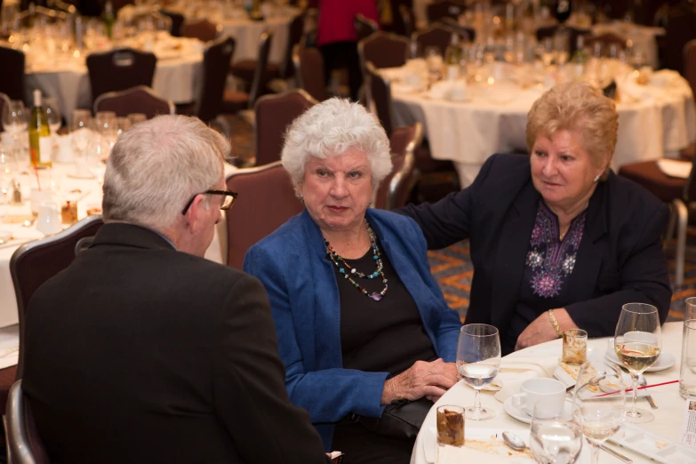 three women sitting at a dinner table and a man standing next to them