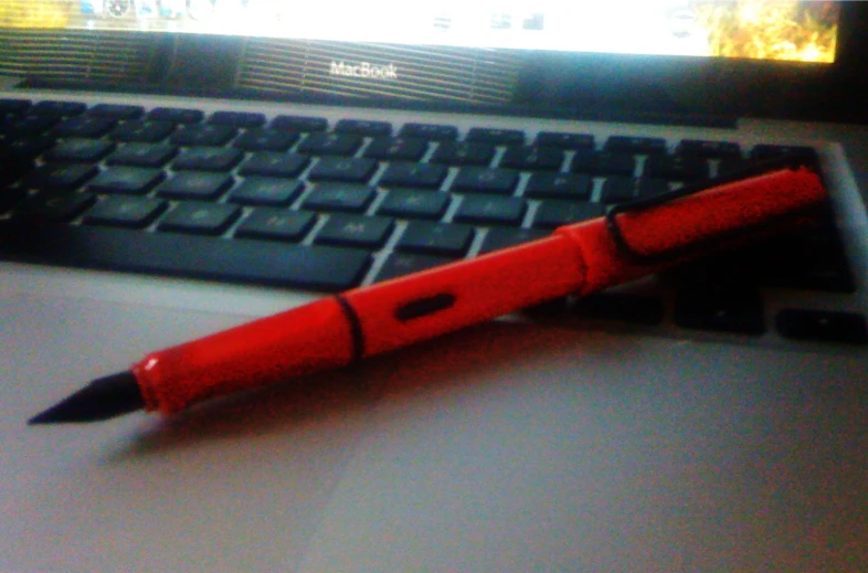 red and black plastic pen resting on a laptop keyboard