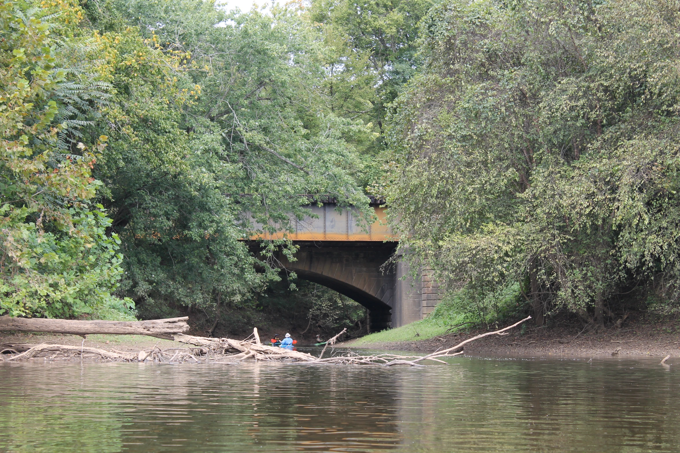 two people in a canoe on a river under a bridge