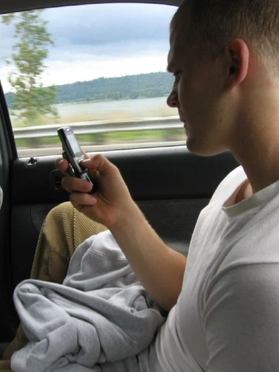 a young man sitting in the back of a car looking at a cell phone