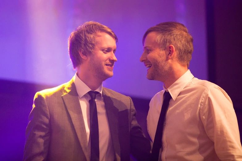 two men wearing suits and ties are smiling together