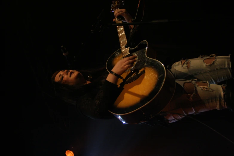 a woman playing an acoustic guitar in front of microphones