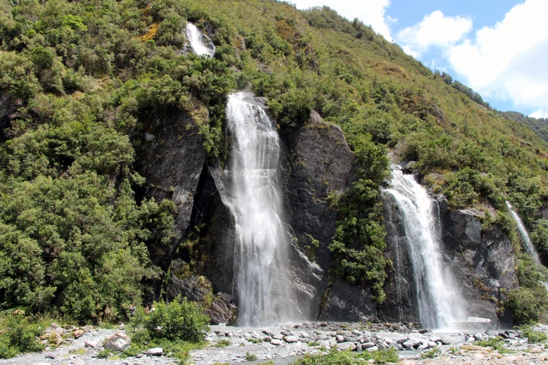 large waterfall with green bushes and rocks on the side