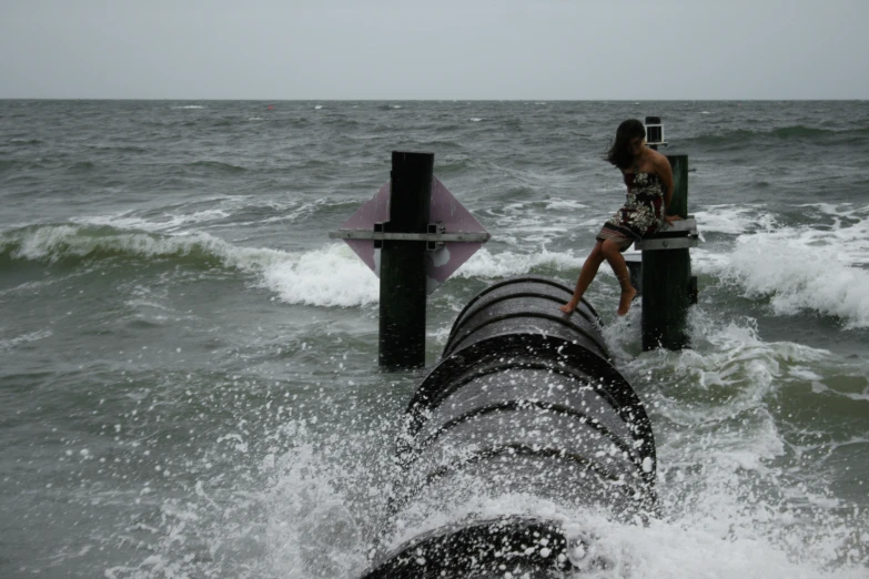 a girl sitting on a pipe that has been washed onto the beach