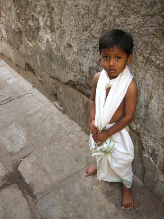 a child in indian attire standing against a stone wall