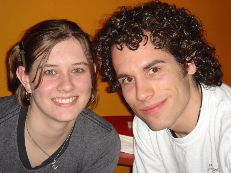 two people posing for the camera in front of a wall