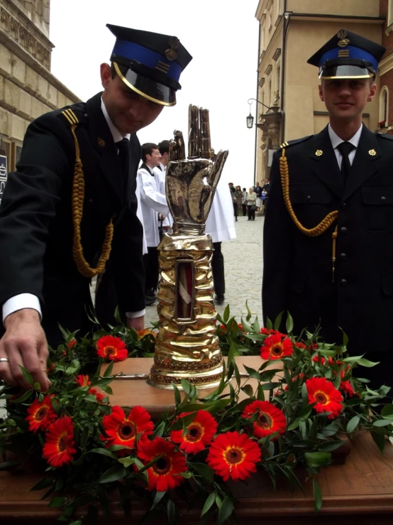 two men in military uniform are placing a gold cup in front of wreaths